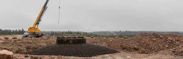 Kuvassa raudoitettu tuulivoimalan jalka, johon betoni valetaan. Raudoituksen sisällä näkyy ihmisiä pienessä koossa. Raudoituksen yläpuolella nosturi.