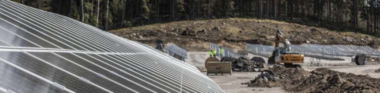 Etualalla aurinkovoimala, taustalla kaivinkone, työntekijöitä ja Rekan kaapelikeloja