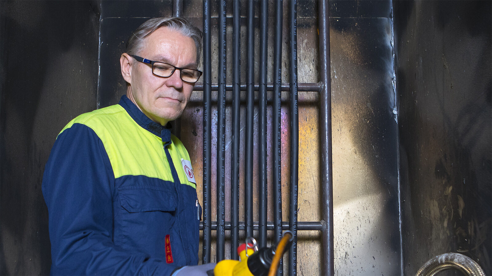 Kuvassa CTC-testikeskuksen silmälasipäinen työntekijä työtakissa on testaamassa kaapeleita polttokaapissa ja painamassa käynnistysnappulaa.