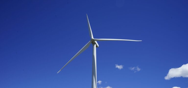 Kuva tuulivoimasta läheltä vasten sinistä taivasta, jossa pari pilvenhattaraa.